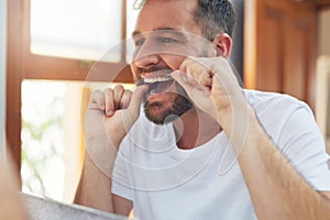 Take your dental hygiene routine a step further by flossing. a handsome young man flossing his teeth in the bathroom.