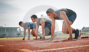 Take your mark. Full length shot of three handsome young male athletes starting their race on a track.