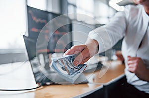 Take your salary. Close up view of woman`s hands that holds money near the monitors with graphs