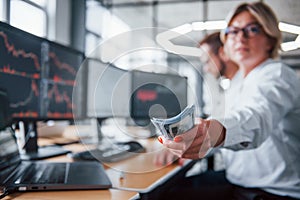 Take your salary. Close up view of woman`s hands that holds money near the monitors with graphs