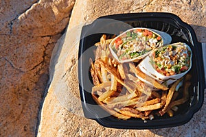 Takeaway food, Fish wrap with french fries, in recyclable plastic container at the isolated rocky ocean beach
