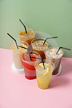 Takeaway glasses of summer drinks with ice. Lemonade and coctails on coloured background.