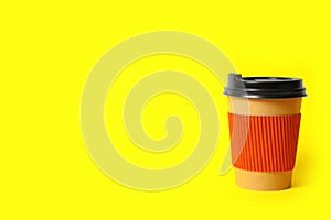 Takeaway paper coffee cup with cardboard sleeve on yellow background. Space for text