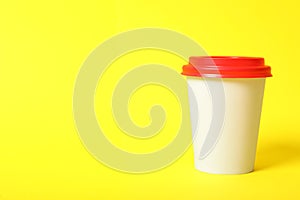 Takeaway paper coffee cup on yellow background, closeup. Space for text
