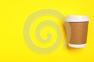 Takeaway paper coffee cup on yellow background, top view. Space for text