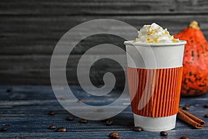 Takeaway paper cup with pumpkin spice latte and whipped cream on wooden table