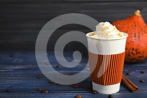 Takeaway paper cup with pumpkin spice latte and whipped cream on wooden table