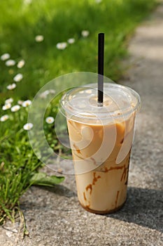 Takeaway plastic cup with cold coffee drink and straw near green grass outdoors