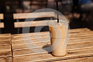 Takeaway plastic cup with cold coffee drink and straw on wooden table outdoors, space for text