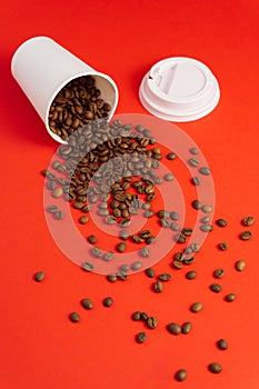Takeaway white paper coffee cup with cap on red background with pouring roasted beans out of it