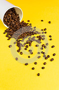 Takeaway white paper coffee cup on yellow background with pouring roasted beans out of it