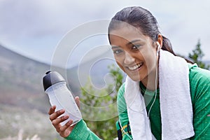 Taking a break from hiking. Portrait of a young woman sitting outdoors with a sports drink while listening to music.