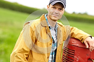 Taking a break. Portrait of a smiling farmer with his arm resting on the hood of his tractor while he stands in an open