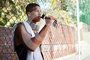 Taking a breather to get some energy. a sporty young man drinking water while standing against a fence outdoors.