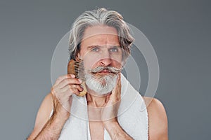 Taking care of face and skin clearness. Stylish modern senior man with gray hair and beard is indoors