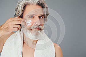 Taking care of face and skin clearness. Stylish modern senior man with gray hair and beard is indoors