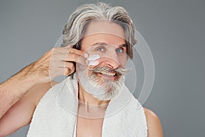 Taking care of face and skin clearness. Stylish modern senior man with gray hair and beard is indoors