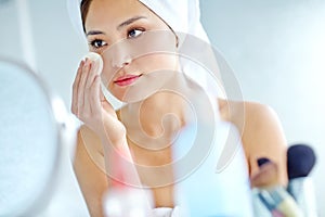 Taking care of her skin. An attactive young Asian woman applying moisturizer with a towel on her head.