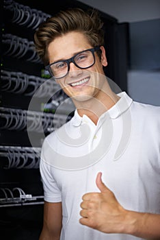 Taking care of your network needs. A happy computer technician in a server room giving you the thumbs up.