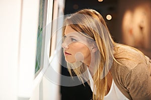 Taking in a century of art. a young woman examining paintings in a gallery.