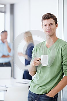 Taking a coffee break. Portrait of a young man in an office holding a cup of coffee.