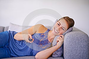 Taking it easy in front of the tv. a young woman watching television while lying on the sofa at home.