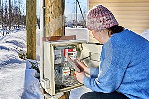 Taking electric meter readings by woman outside in village in winter.