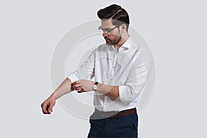 Taking everything seriously. Good looking young man in formalwear adjusting his sleeve while standing against grey background