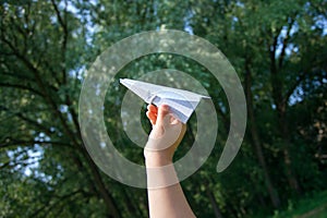 Taking flight! Hand holding paper airplane in the sky and green garden, concept of summer, childhood, dreaming.