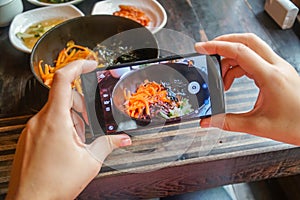 Taking Food Photo of Traditional Korean Dish Bibimbap Served Along With Small Side Dishes Clled Banchan on Mobile Phone