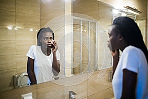 Taking good care of her face. Beautiful young African woman cleaning her face with sponge and smiling while standing against a