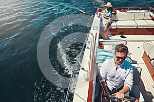 Taking her out onto the open seas. High angle shot of a handsome young man steering a yacht with his wife sitting in the