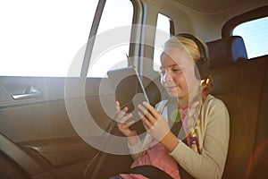 Taking her tablet along for the ride. a little girl traveling in a car.