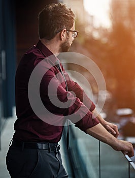 Taking a minute to breakaway from business. a young businessman standing outside on the balcony of an office.