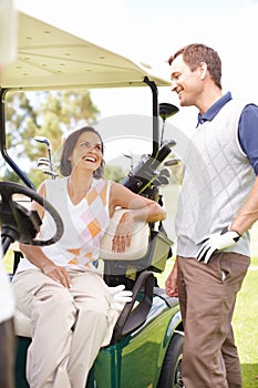 Taking a moment to relax between holes. Smiling woman seated in a golf cart with her husband standing alongside her.