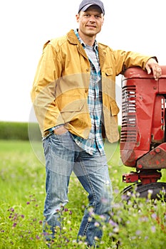 Taking a moment to relax. Portrait of a man standing in a field with his arm resting on the hood of a tractor.