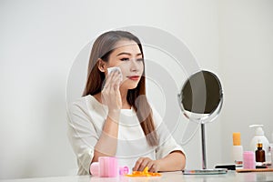 Taking off her make-up. Beautiful cheerful young woman using cotton disk and looking at her reflection in mirror with smile while