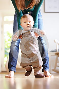 Taking one step at a time. Young mom helping her baby boy learn to walk.