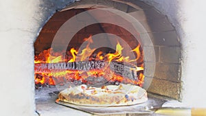 Taking out tasty pizza from oven in a wood oven