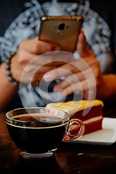 Taking photo with black coffee and red velvet cake on dark wooden table with smartphone with man hand. for up to social network.