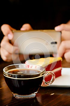 Taking photo with black coffee and red velvet cake on dark wooden table with smartphone with man hand. for up to social network.