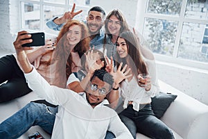 Taking a picture. Cheerful young friends having fun and drinking in the white interior