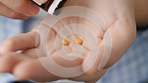Two small orange round pills fall into palm of hand from pill bottle. Close-up, front view, center composition