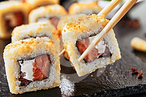 Taking portion of hot crispy tempura maki sushi rolls with cream cheese, raw salmon, tomato and nori seaweed.