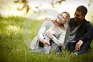 Taking a quiet moment to laugh. a loving young couple sitting on the grass in a park.