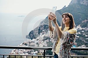 Taking selfie with smartphone fornt camera.Smiling young woman traveler enoying seaview in Positano,Italy. Vacation on Amalfi