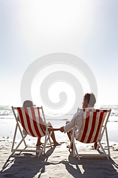 Taking in the stunning view. Rearview of a happy couple sitting on deck-chairs on the beach and holding hands.