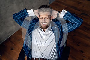 Taking time for a minute break. Cheerful young man holding hands behind head and keeping eyes closed while sitting at his working