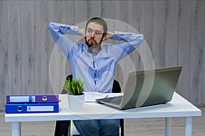 Taking time for a minute break. Cheerful young man holding hands behind head and keeping eyes closed while sitting at his working