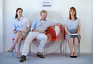 Taking up space. Two job candidates looking disgustedly at a young man sprawled on the chairs next to them.